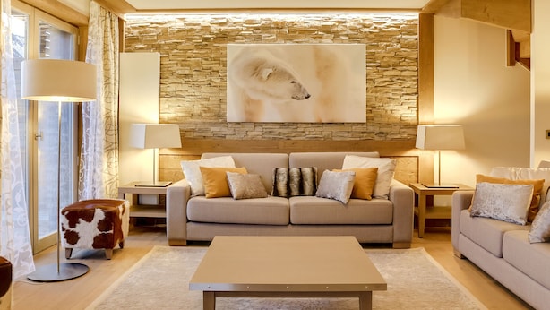 Una sala de estar acogedora con una pared de piedra, un cuadro abstracto grande y un sofá beige con muchos cojines.