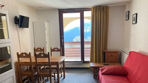 Une pièce comprenant une table à manger, des chaises, un canapé rouge, un téléviseur, une porte-fenêtre coulissante et un petit meuble.