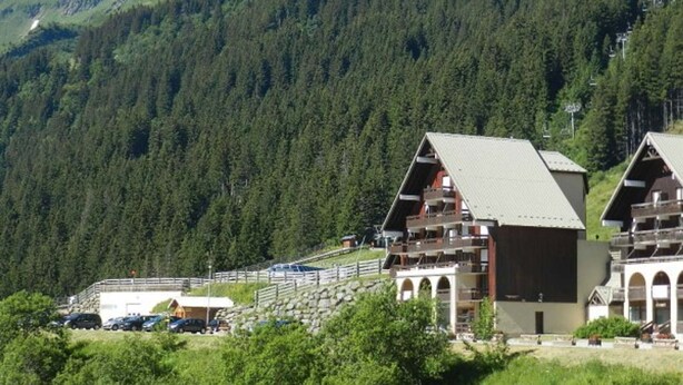Un chalet de montagne doté de plusieurs balcons, avec un télésiège visible en arrière-plan.