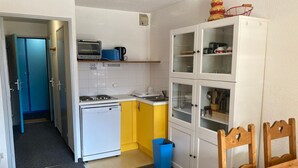 Une cuisine compacte équipée d’un four à micro-ondes, d’un grille-pain et d’une cuisinière, ainsi que d’une petite poubelle et d’un coin repas avec une table et des chaises en bois.