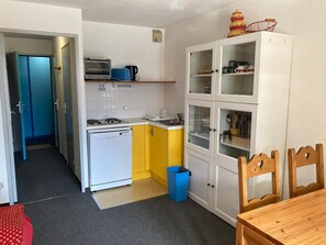A compact kitchen with a microwave, toaster, and stove, a small trash bin, and a dining area with a wooden table and chairs.