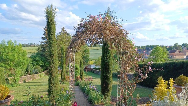 Un sentier de jardin menant à une pergola en bois recouverte de plantes grimpantes.