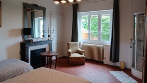 Une chambre d’hôtel avec une cheminée, une grande fenêtre avec des rideaux, un fauteuil et un lit.