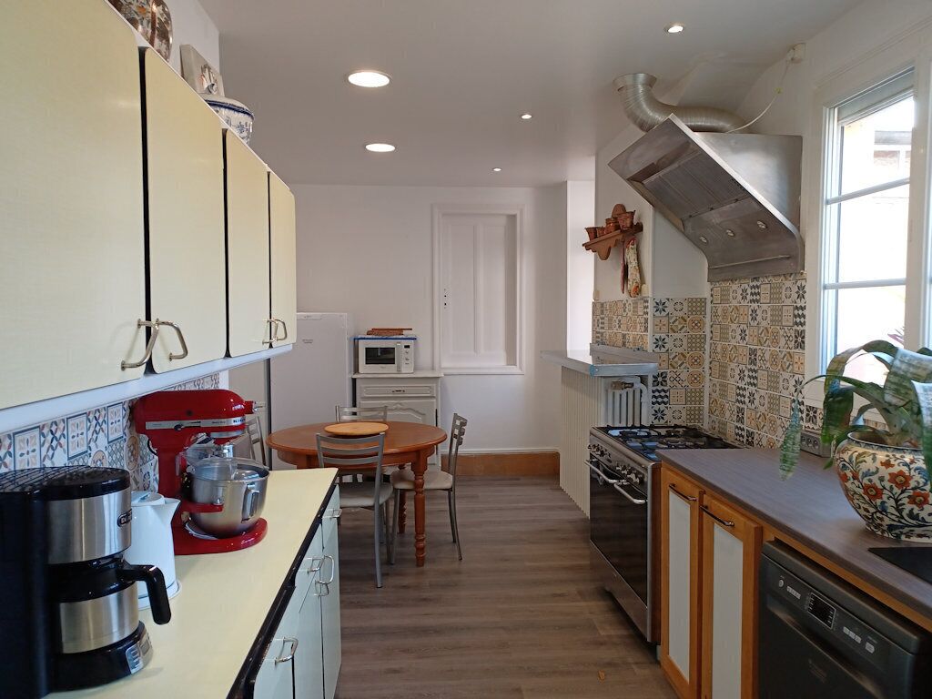 A kitchen with white cabinets, a red mixer, a stove, and a dining table with chairs.