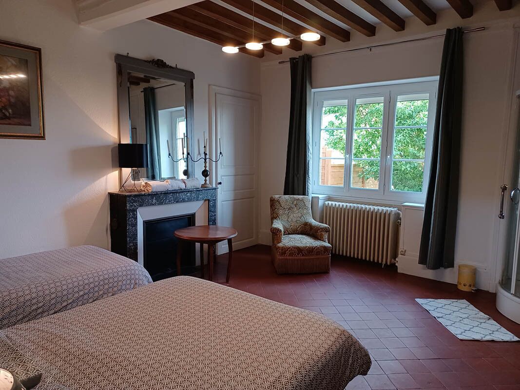 Ein Schlafzimmer mit zwei Betten, einem Kamin, einem Fenster mit Blick auf Grünflächen und einem Sessel.