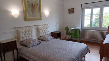 A bedroom with a large bed, a chair, a table, and a window with a view.