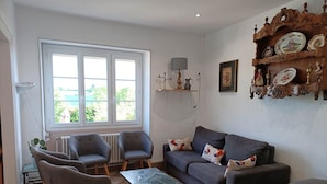 Un salon avec un canapé gris, deux fauteuils, une table basse et une fenêtre donnant sur un beau paysage.