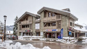 A modern building with a stone facade, multiple balconies, and a sign for 'INTERSPORT'. - Charming apartment in Courchevel Village, near slopes, WIFI, parking included (Courchevel 1550)