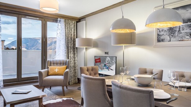 A modern hotel room with a dining area, two armchairs, a sofa, a coffee table, and a TV displaying a sports event. - Charming apartment in Courchevel Village, near slopes, WIFI, parking included (Courchevel 1550)