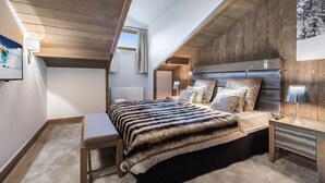 A bedroom with a sloped ceiling, wooden walls, a bed with a fur throw, a bench, and a nightstand with a lamp. - Charming apartment in Courchevel Village, near slopes, WIFI, parking included (Courchevel 1550)