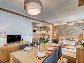 A modern living room with a dining area, a TV, and a stone wall.