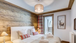 Un dormitorio con pared de madera, cama con ropa de cama blanca y almohadas a rayas, mesita de noche con lámpara e imagen enmarcada de un ciervo en la pared.