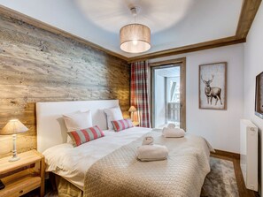 Una camera da letto con parete in legno, un letto con biancheria bianca e cuscini a righe, un comodino con lampada e un quadro di un cervo appeso al muro.