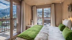 Ein Schlafzimmer mit einem großen Bett, Blick auf einen verschneiten Berg und einem Balkon mit Holzgeländer.