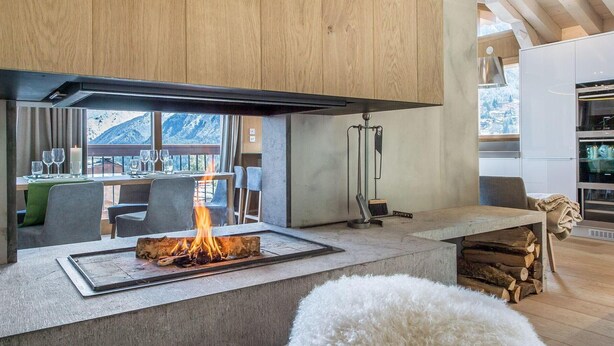 Eine moderne Küche mit integriertem Kamin, Holzschränken und Bergblick durch große Fenster.