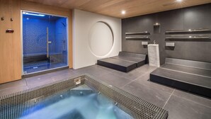 Ein moderner Wellnessraum mit Holzboden, einer blauen Duschkabine, einer runden Wandverkleidung und einer Sitzecke mit Marmorwaschbecken.