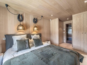 Quarto moderno com cama grande, duas luminárias pendentes, guarda-roupa e elevador.