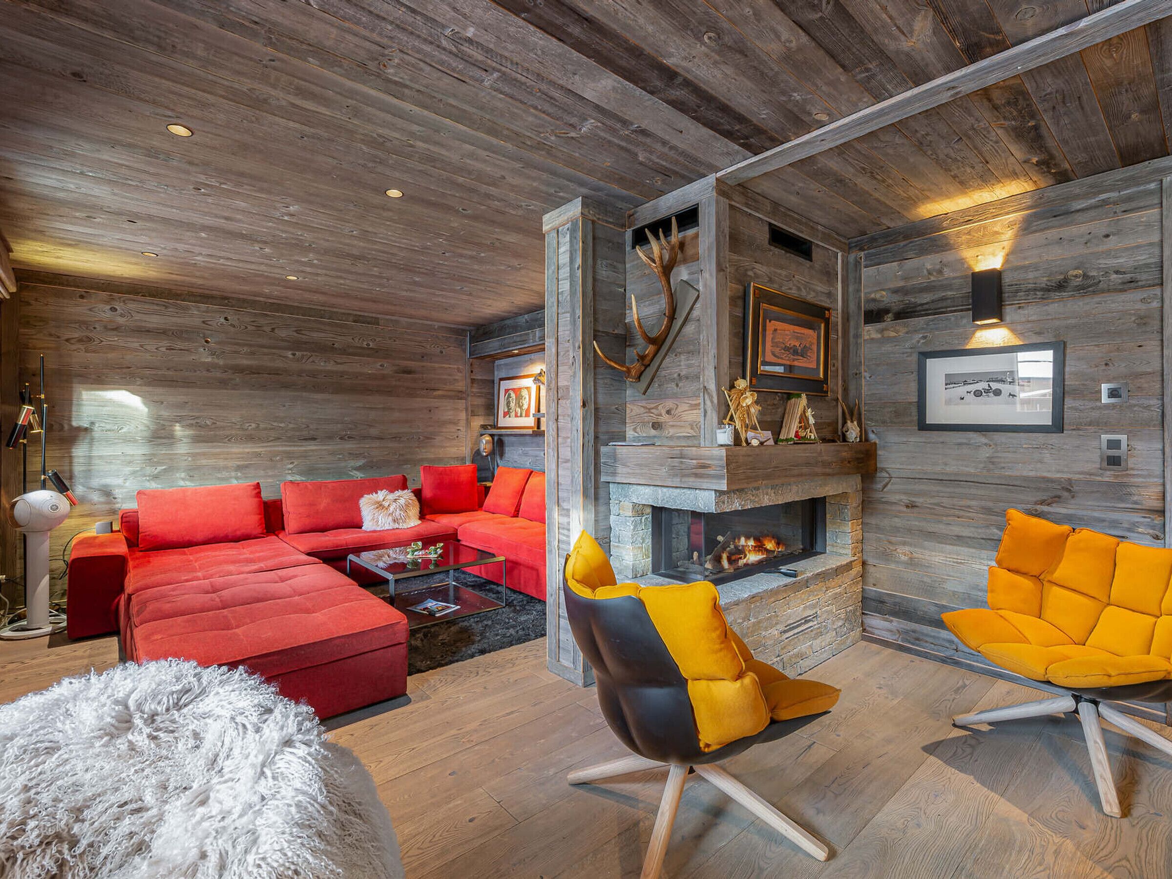 A modern living room with a red sectional sofa, a black and yellow chair, a white fluffy rug, and a fireplace.
