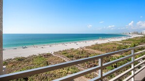 A beach with a wooden walkway, clear blue water, and buildings in the background.