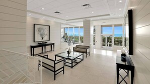 A spacious living area with a large window offering a view of the ocean, a modern fireplace, and a dining area with a glass table.