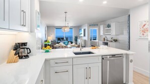 A modern kitchen with white cabinetry, a central island with a sink, and a view of the sea through large windows.