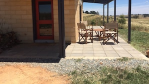 Une terrasse couverte avec des meubles d’extérieur, une porte rouge et une vue sur un champ verdoyant.