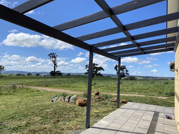 A covered outdoor area with a view of a grassy field and distant hills. - Rural retreat and family friendly (Orange)