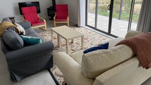 Un salon comprenant un canapé, des fauteuils, un téléviseur et une vue sur l’extérieur, accessible par une porte vitrée.
