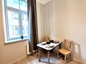 Un comedor con una mesa dispuesta para dos personas, una ventana con cortinas y un radiador.