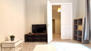 Ein schlicht eingerichtetes Wohnzimmer mit Fernseher, einem kleinen Tisch und einem Bücherregal.