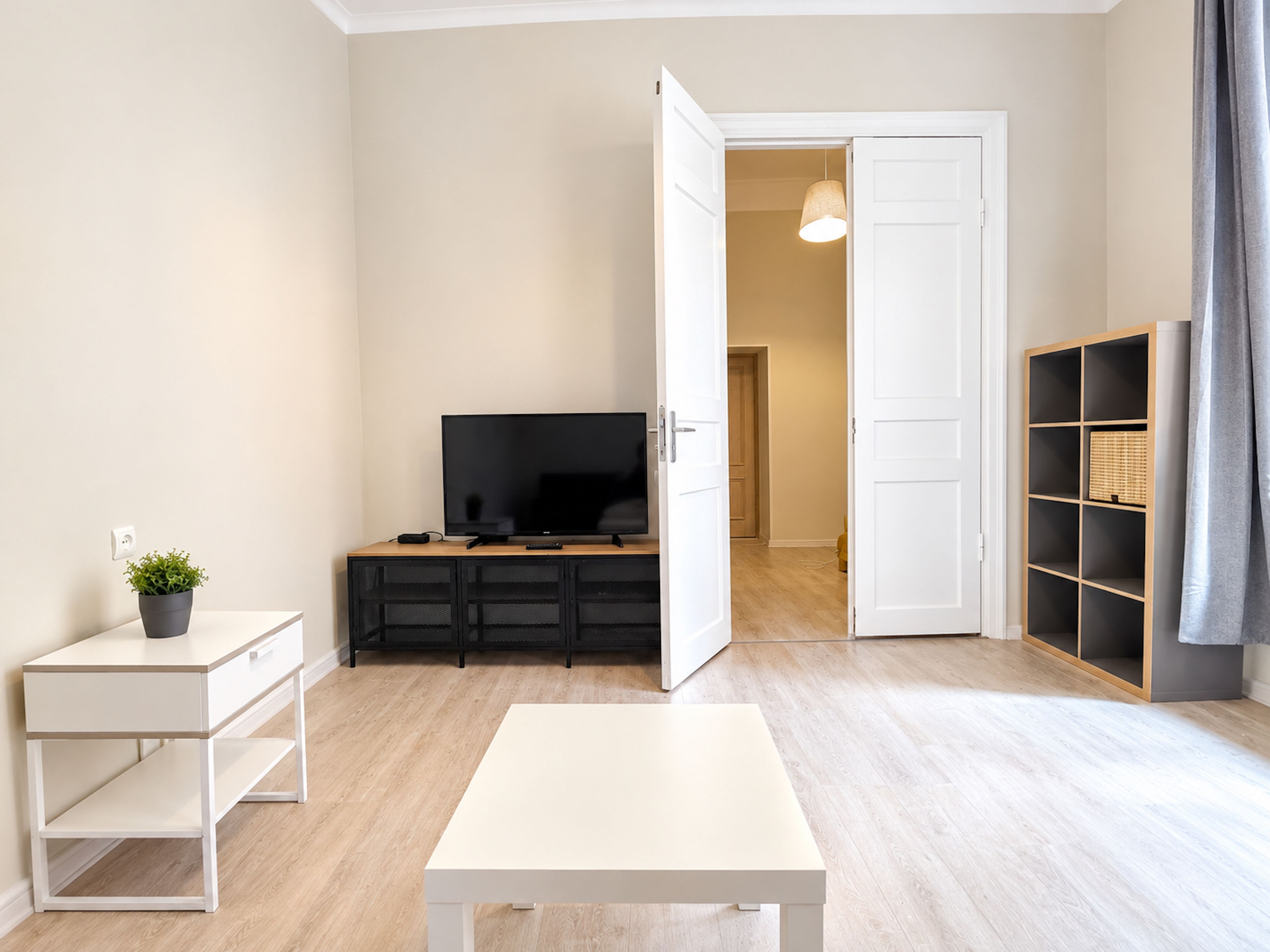 Ein minimalistisches Wohnzimmer mit Flachbildfernseher, einem kleinen Tisch und einem Bücherregal.