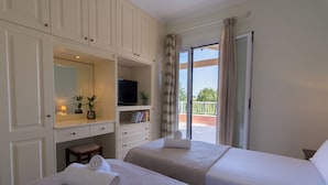 Une chambre d’hôtel avec deux lits, une télévision, une petite table avec une plante et un balcon avec vue.