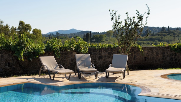 Une piscine avec trois chaises longues et un mur de pierre en arrière-plan.