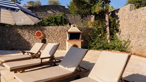 Un espace aménagé au bord de la piscine, avec des chaises longues et un barbecue.