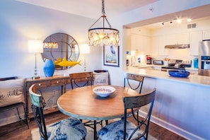 Una cocina moderna con armarios blancos, un refrigerador de acero inoxidable y un comedor con mesa y sillas de madera.