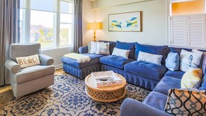 Uma sala de estar com uma poltrona cinza, um sofá modular azul, um tapete estampado e uma mesa de centro redonda de madeira.