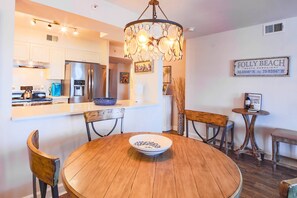 A modern kitchen with stainless steel appliances, a wooden dining table with a bowl, and a decorative chandelier.