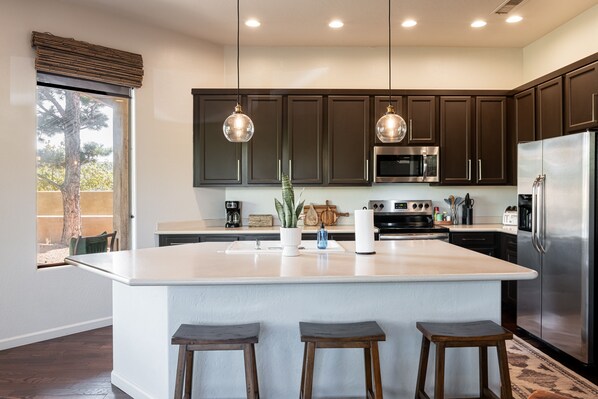Una cocina moderna con armarios oscuros, una isla grande con taburetes, electrodomésticos de acero inoxidable e iluminación colgante.