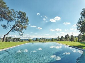 Una piscina rectangular con agua azul cristalina, rodeada por un césped cuidado y árboles.