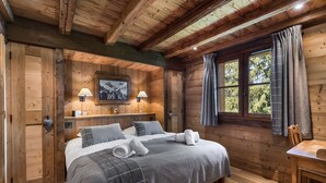 Une chambre dans une cabane en bois, avec un lit, des lampes de chevet, une fenêtre avec des rideaux et une table en bois.