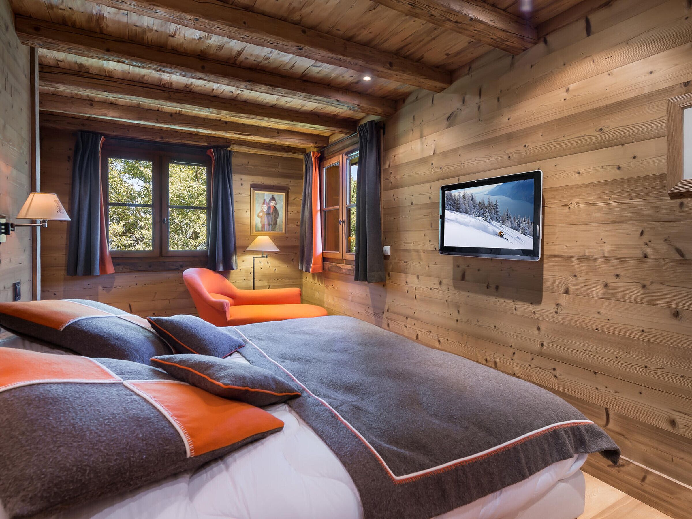 Une pièce chaleureuse, aménagée dans un chalet en bois, avec un lit, une chaise, un téléviseur et une fenêtre avec des rideaux.