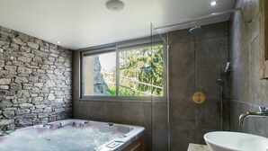 Une salle de bain moderne avec un mur en pierre, une grande baignoire, une douche et un meuble-lavabo en bois.