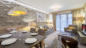 Un salon moderne avec un mur en pierre, un canapé, une table à manger pour quatre personnes et un pouf en peau de vache marron et blanche.