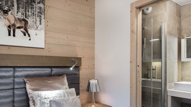 Une chambre moderne avec une tête de lit en bois, un lit confortable, une table de chevet avec une lampe et une cabine de douche en verre.