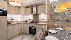 Une cuisine moderne avec des meubles en bois, un four encastré et un coin repas agrémenté d’un mur en pierre.