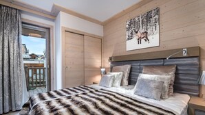 Une chambre à coucher avec un grand lit, une tête de lit en bois, un tableau représentant un cerf et une porte coulissante donnant sur un balcon.