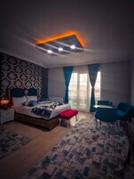 A modern bedroom with a large bed, a bedside table, a chair, and a view of the outside.