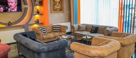 A modern living room with a TV, comfortable sofas, a fireplace, and a large window with curtains.
