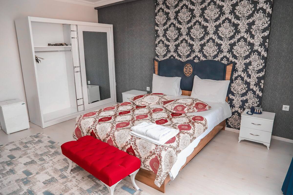 Un dormitorio con cama, un banco rojo, un armario, una mesita de noche y un papel tapiz estampado.