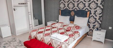Un dormitorio con cama, un banco rojo, un armario, una mesita de noche y un papel tapiz estampado.